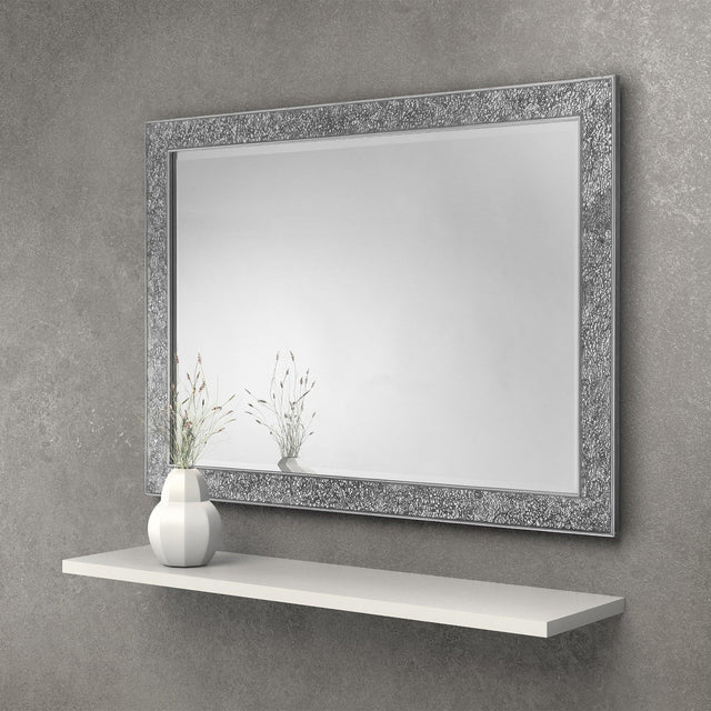 Rectangular wall mirror with decorative silver textured frame above a white floating shelf