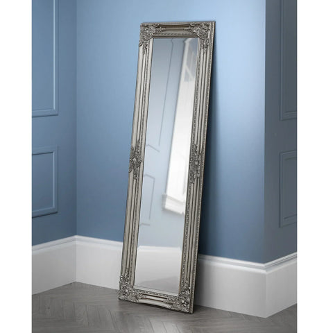Full length pewter dress mirror with ornate frame leaning against blue paneled wall