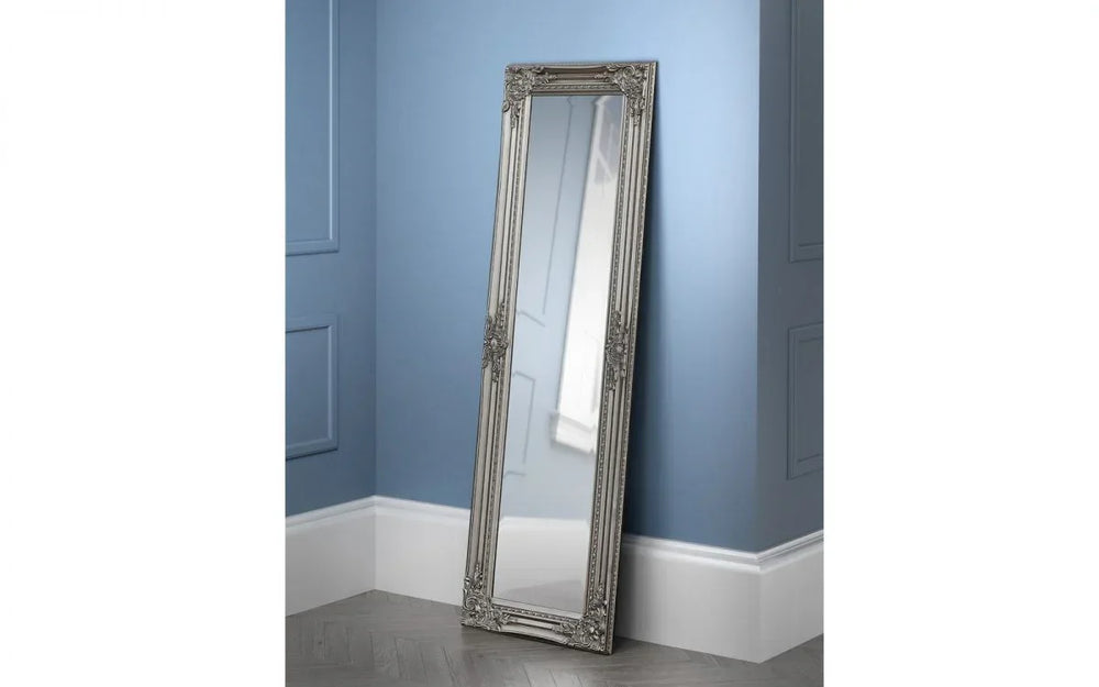 Ornate silver full length mirror with decorative frame leaning against a blue wall
