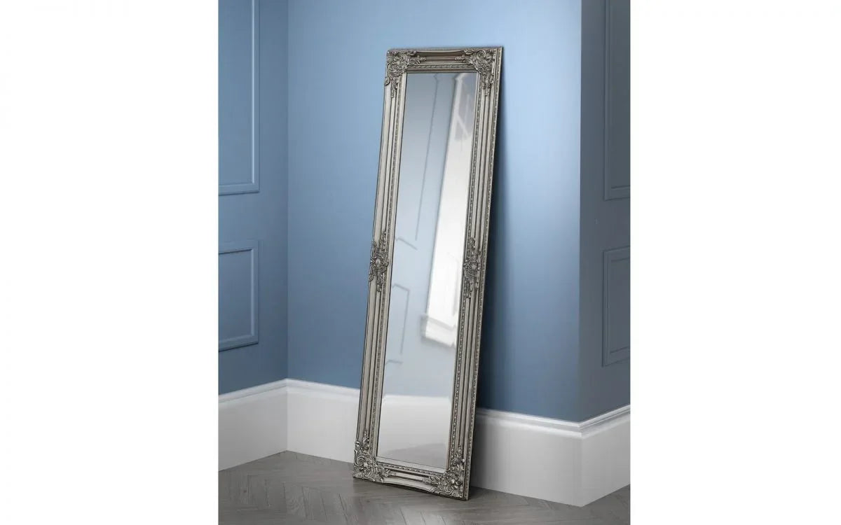 Ornate silver full length mirror with decorative frame leaning against a blue wall