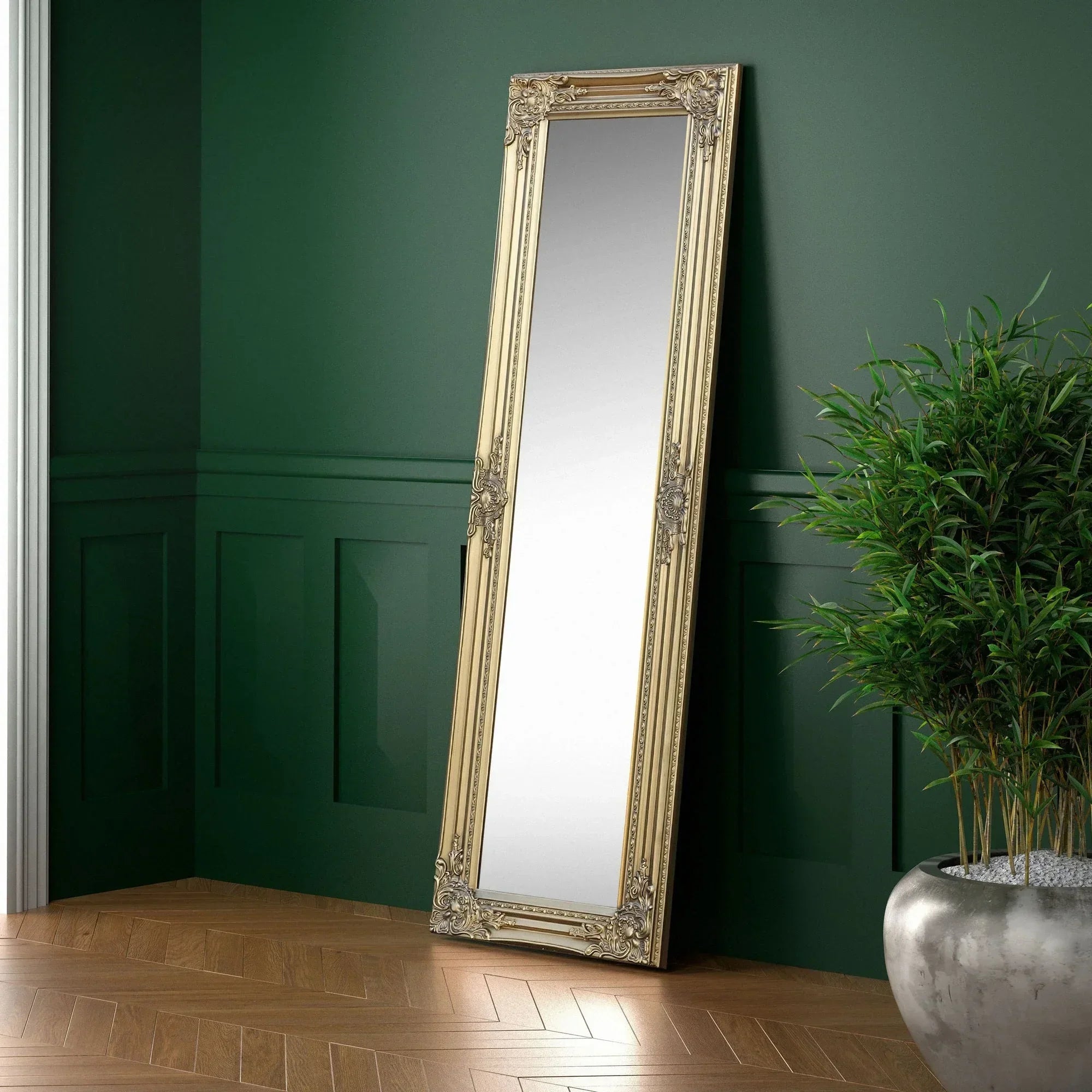 Gold ornate full length mirror with carved frame leaning against dark green wall