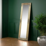 Gold ornate full length mirror with carved frame leaning against dark green wall