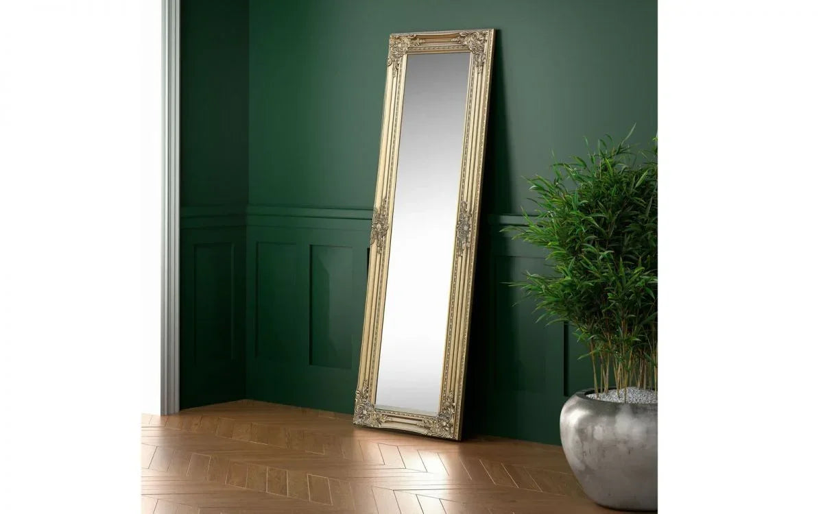 Gold ornate full length mirror leaning against green wall beside silver plant pot