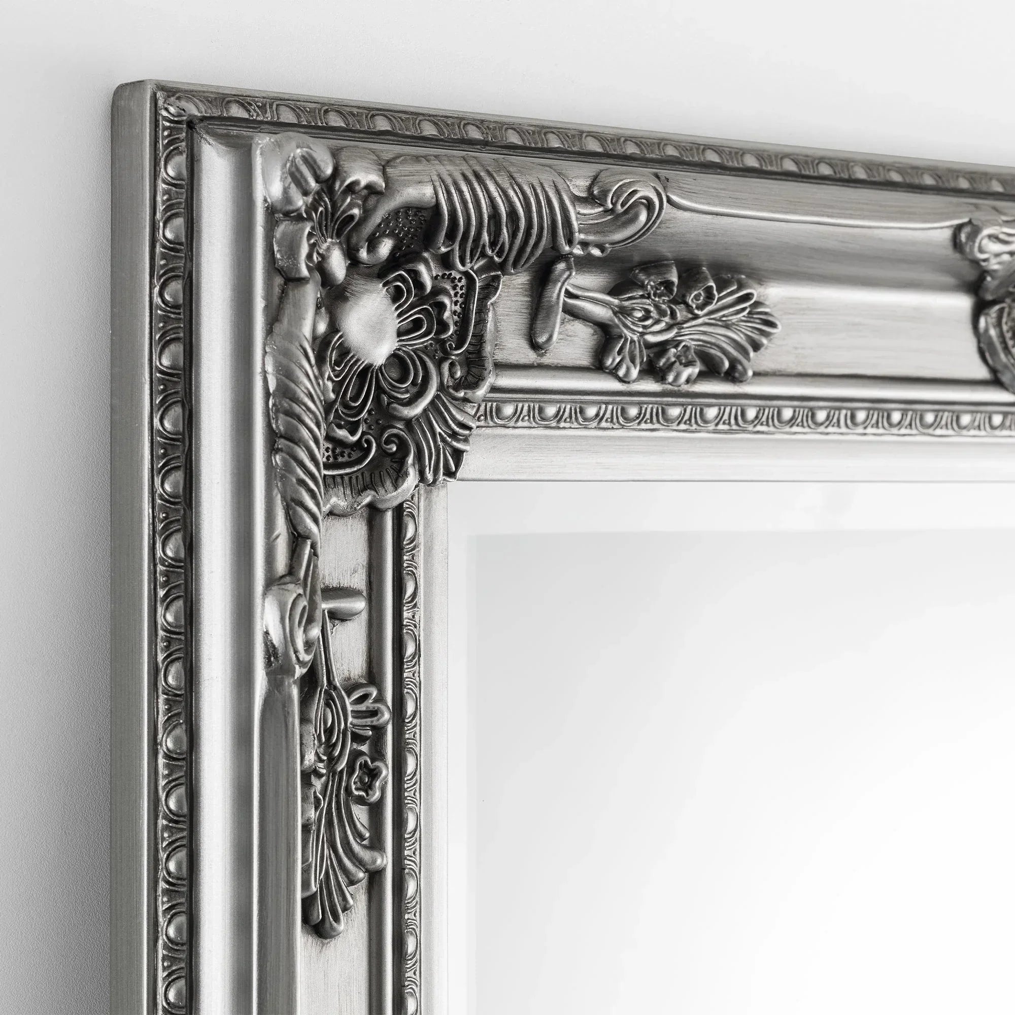 Pewter dress mirror with ornate carved frame detail shown close up against a white wall