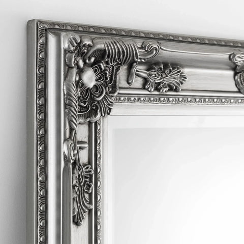 Pewter dress mirror with ornate carved frame detail shown close up against a white wall
