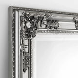 Pewter dress mirror with ornate carved frame detail shown close up against a white wall