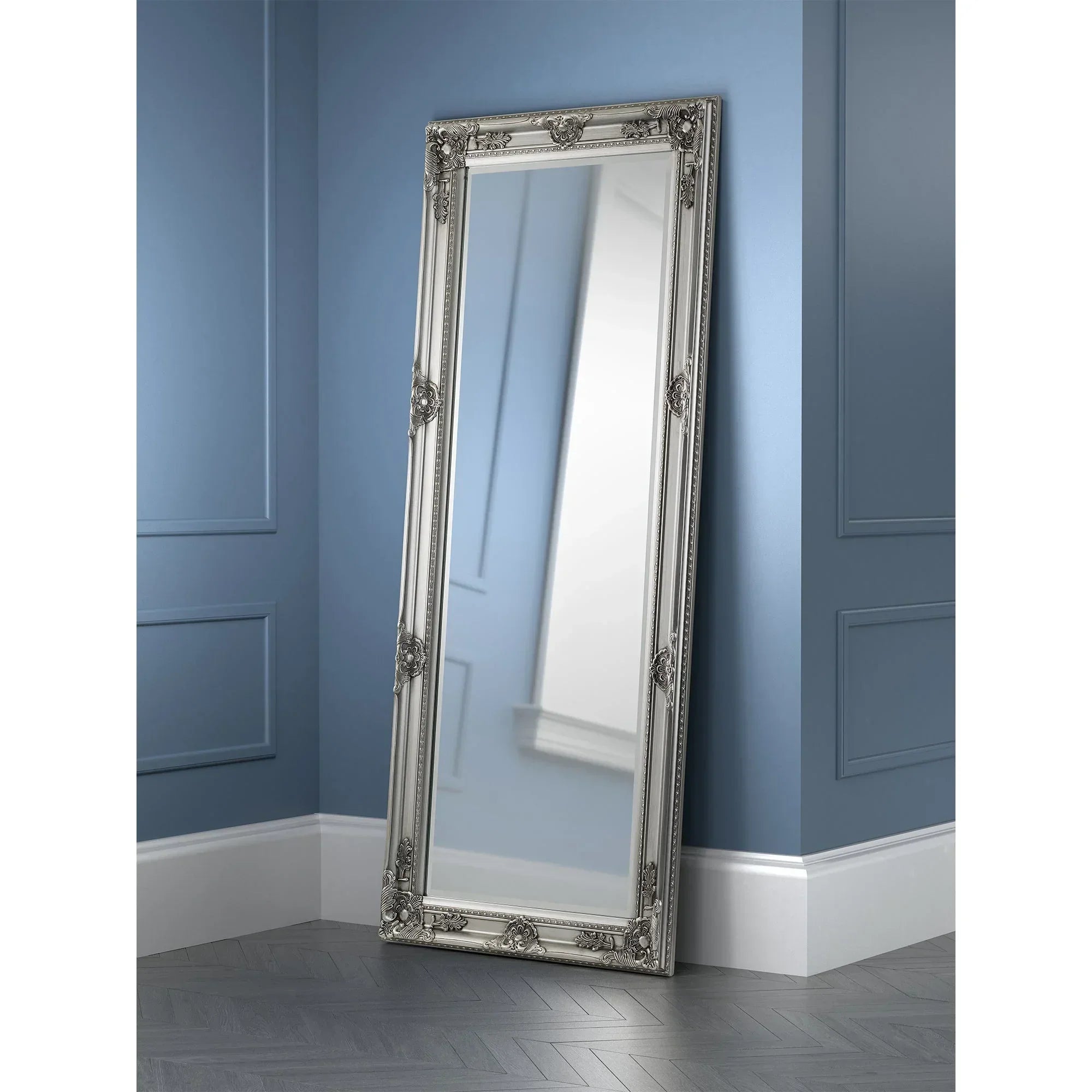 Pewter lean-to dress mirror with ornate frame against blue paneled wall and herringbone floor