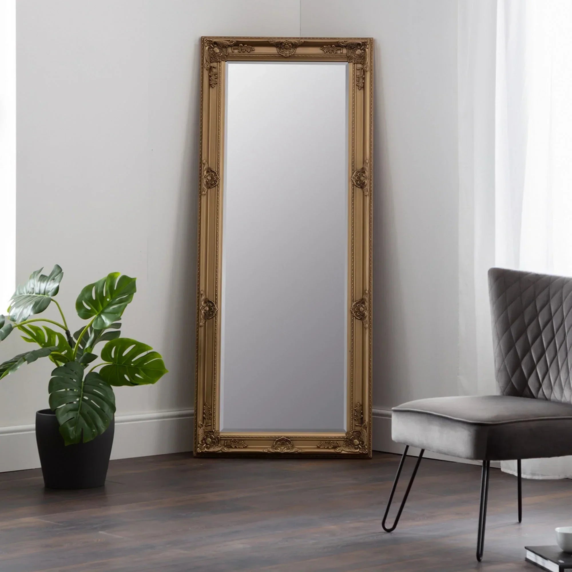 Gold ornate full length mirror leaning against wall in modern living room with dark wood floor