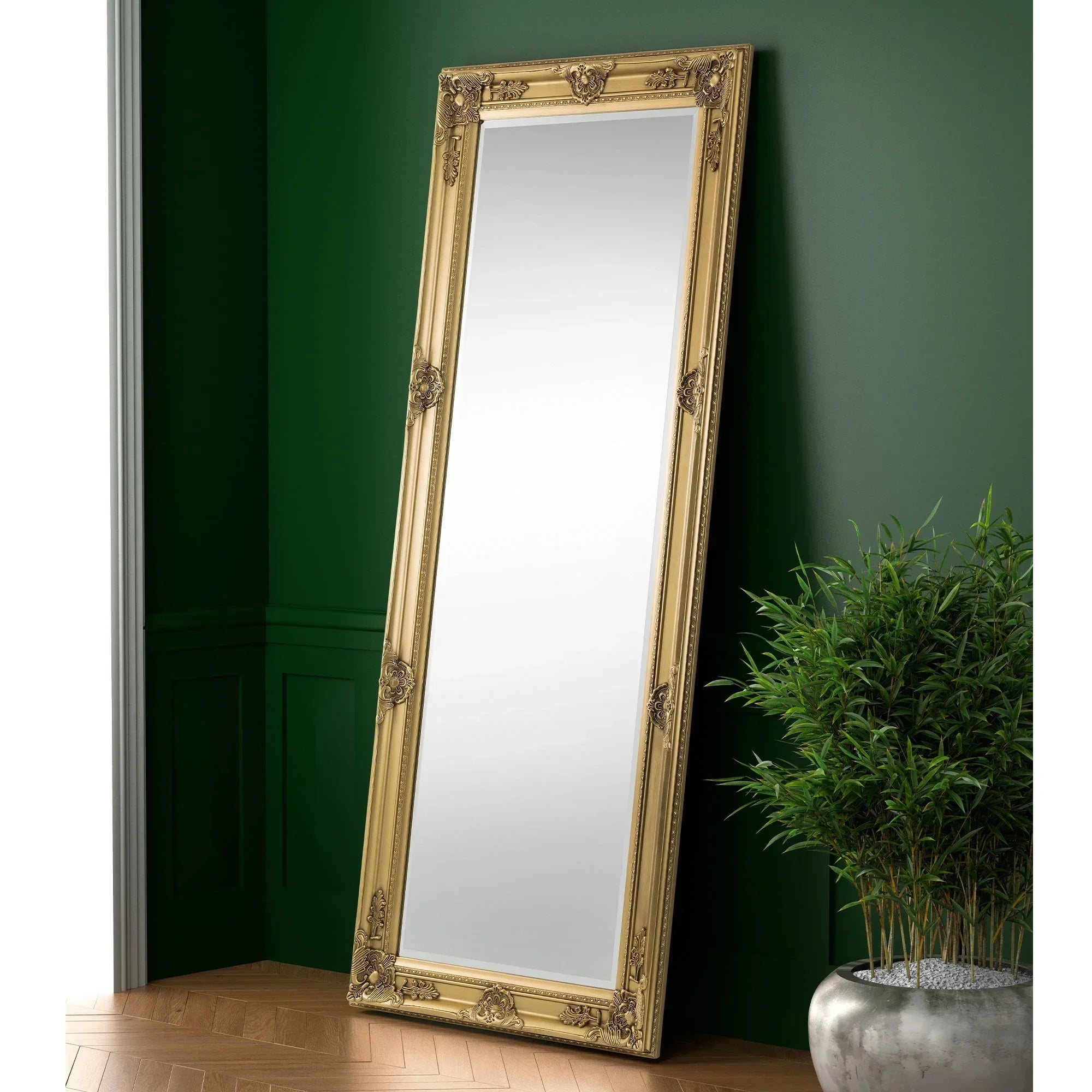 Gold ornate dress mirror leaning against green wall beside potted plant on wooden floor