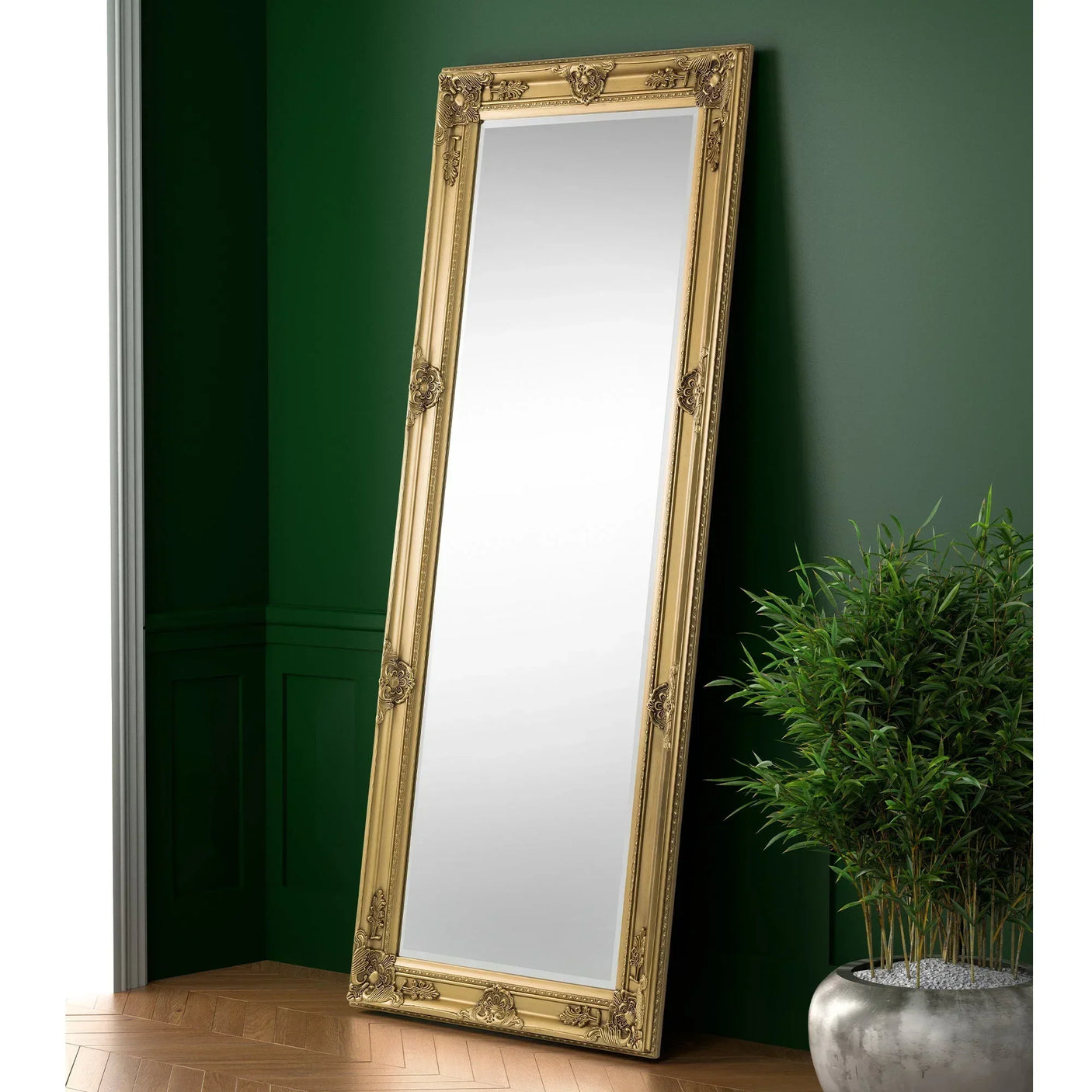 Gold ornate dress mirror leaning against green wall beside potted plant on wooden floor