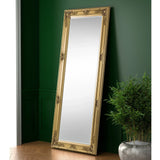 Gold ornate dress mirror leaning against green wall beside potted plant on wooden floor