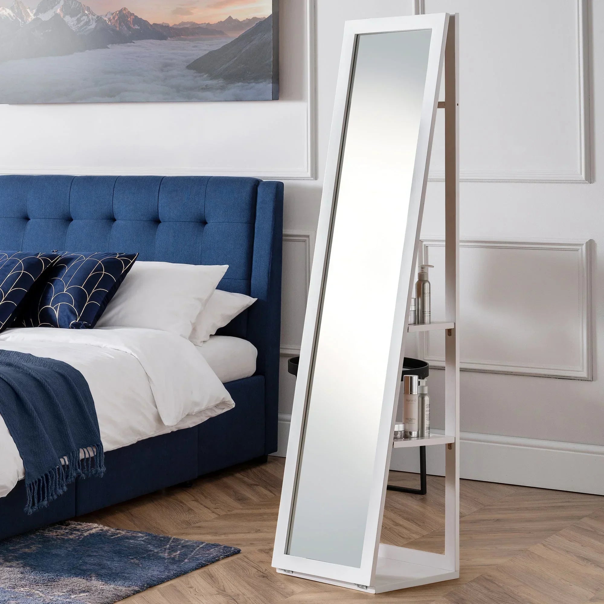 White storage mirror with shelving angled beside blue bed in modern bedroom