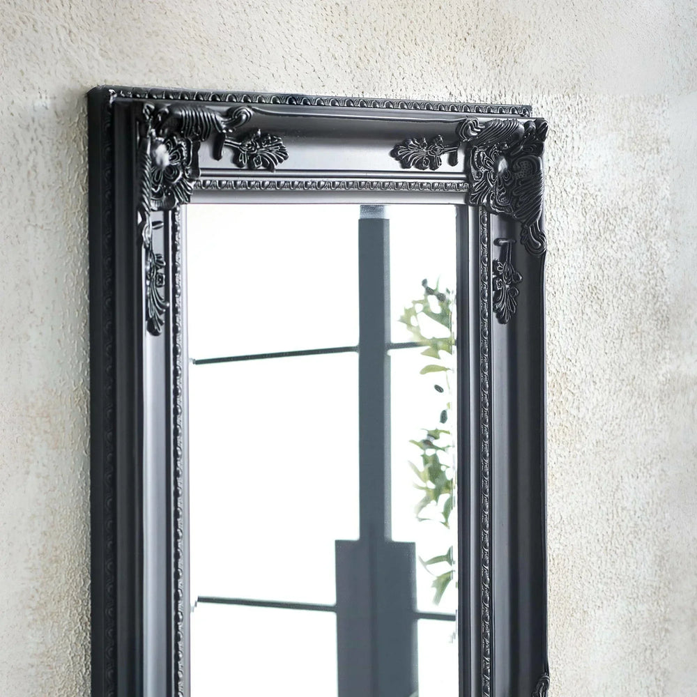 Black ornate wall mirror with decorative frame detailing hung on textured wall