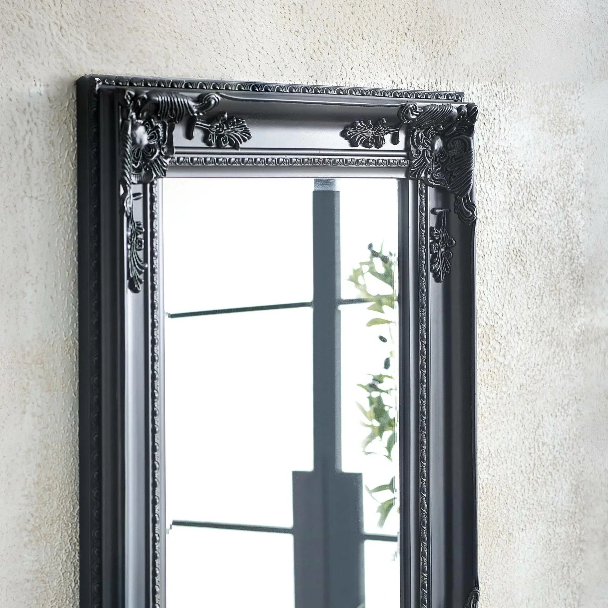 Black ornate wall mirror with decorative frame detailing hung on textured wall