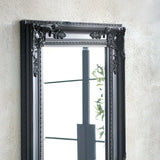 Black ornate wall mirror with decorative frame detailing hung on textured wall