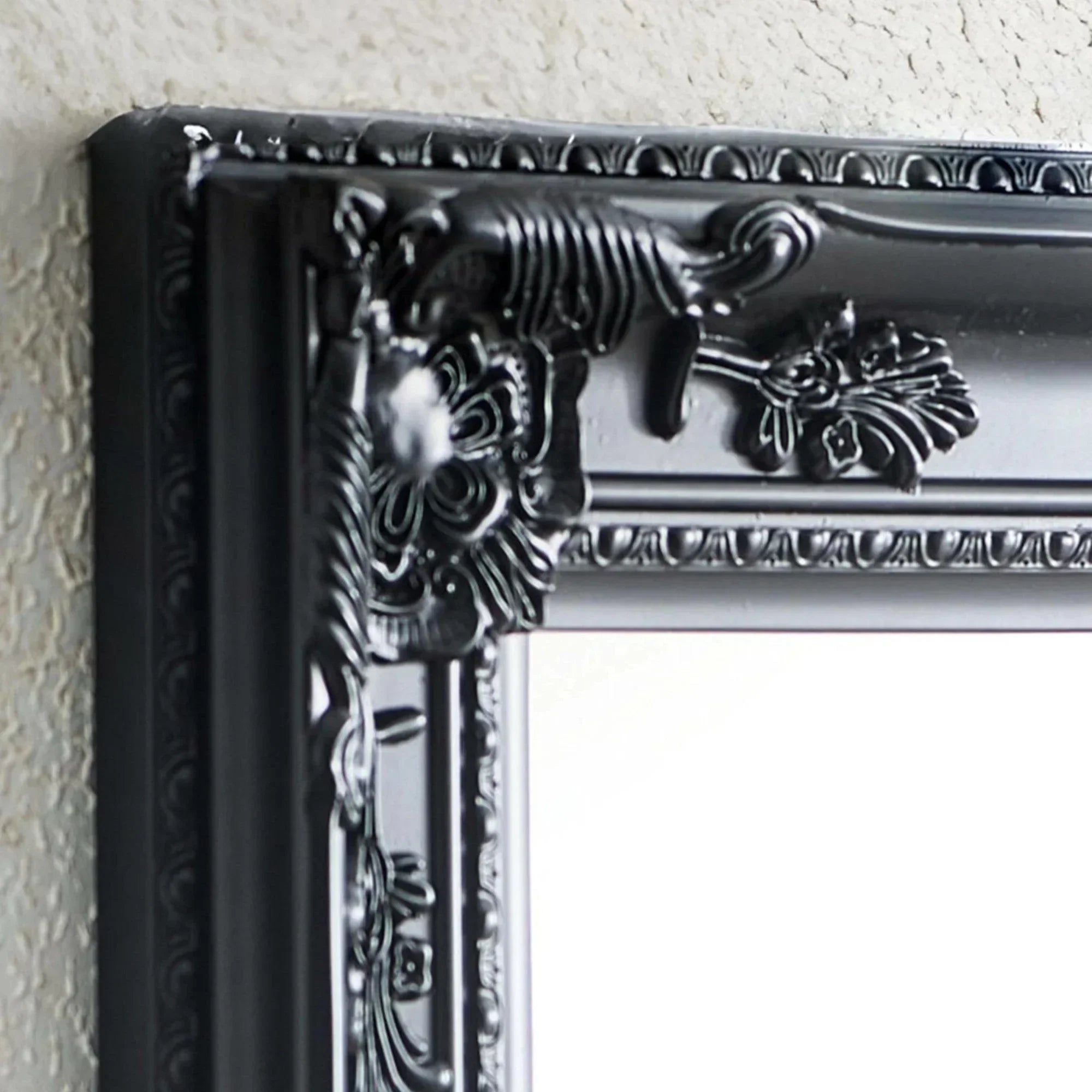 Close-up of black ornate mirror frame with floral detailing on textured wall