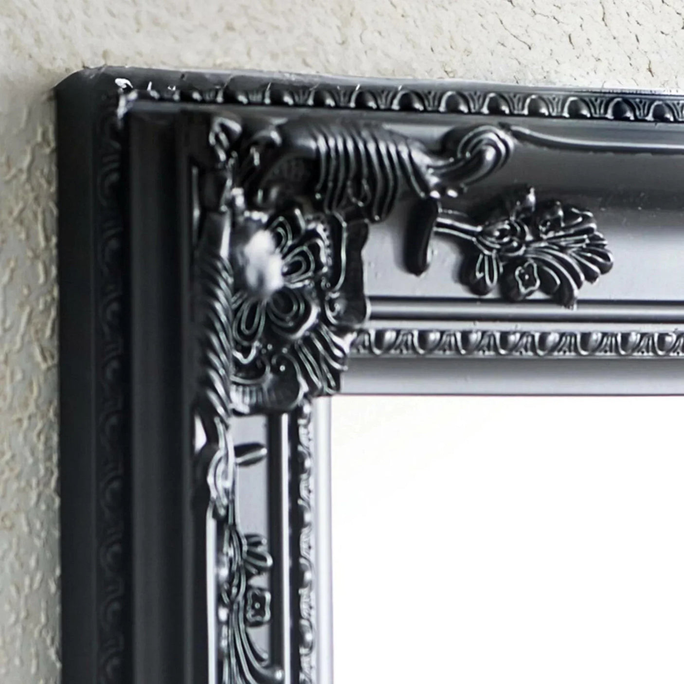 Close-up of black ornate mirror frame with floral detailing on textured wall