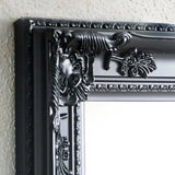 Close-up of black ornate mirror frame with floral detailing on textured wall