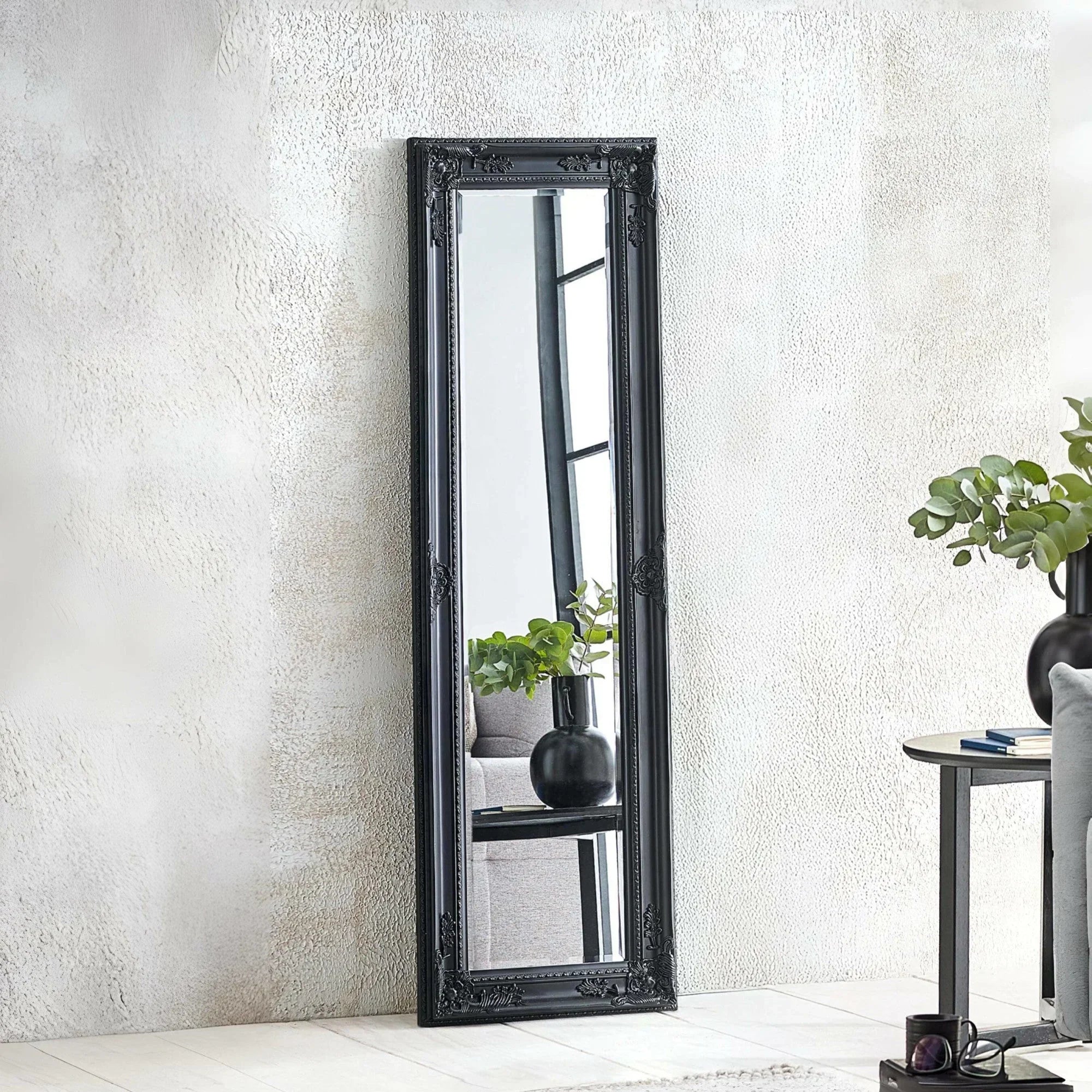 Black ornate full length mirror leaning against textured wall in modern living room