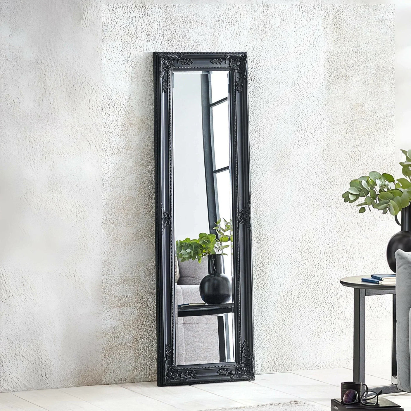 Black ornate full length mirror leaning against textured wall in modern living room