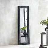 Black ornate full length mirror leaning against textured wall in modern living room