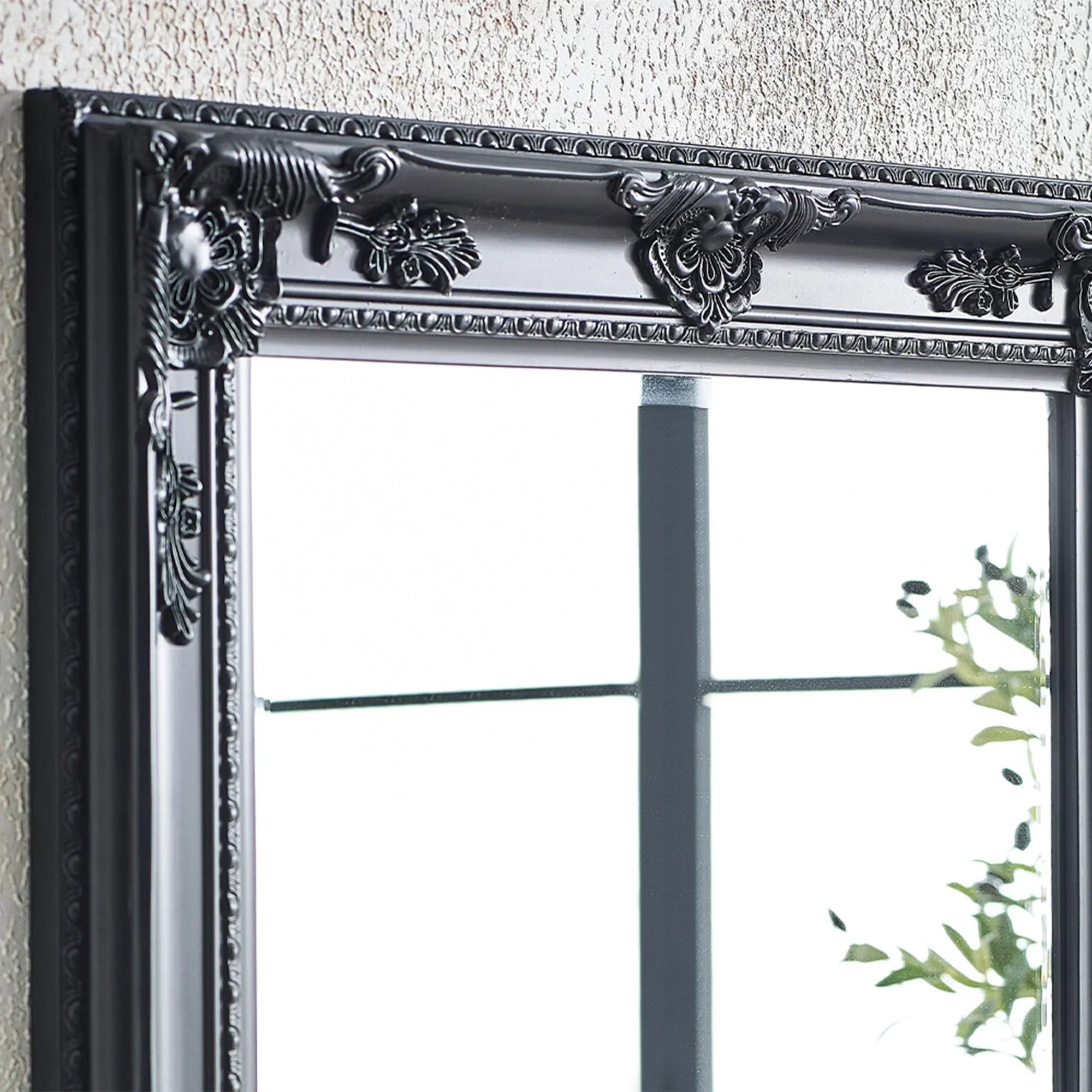 Black ornate mirror frame with decorative floral detailing against textured wall
