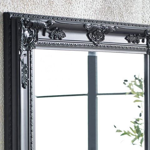 Black ornate mirror frame with decorative floral detailing against textured wall