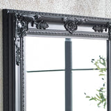 Black ornate mirror frame with decorative floral detailing against textured wall