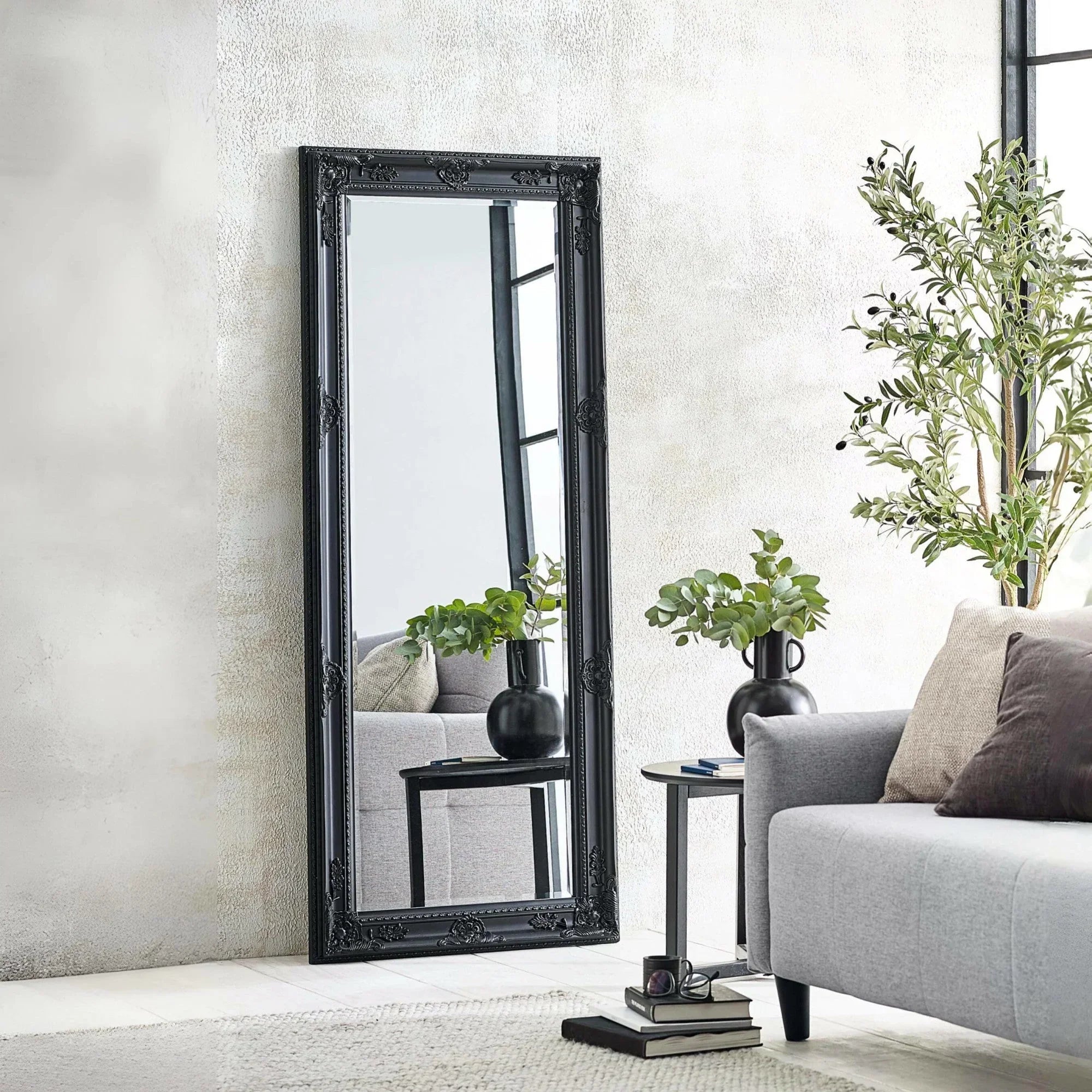 Black ornate full length mirror leaning against wall in modern living room with grey sofa