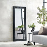 Black ornate full length mirror leaning against wall in modern living room with grey sofa