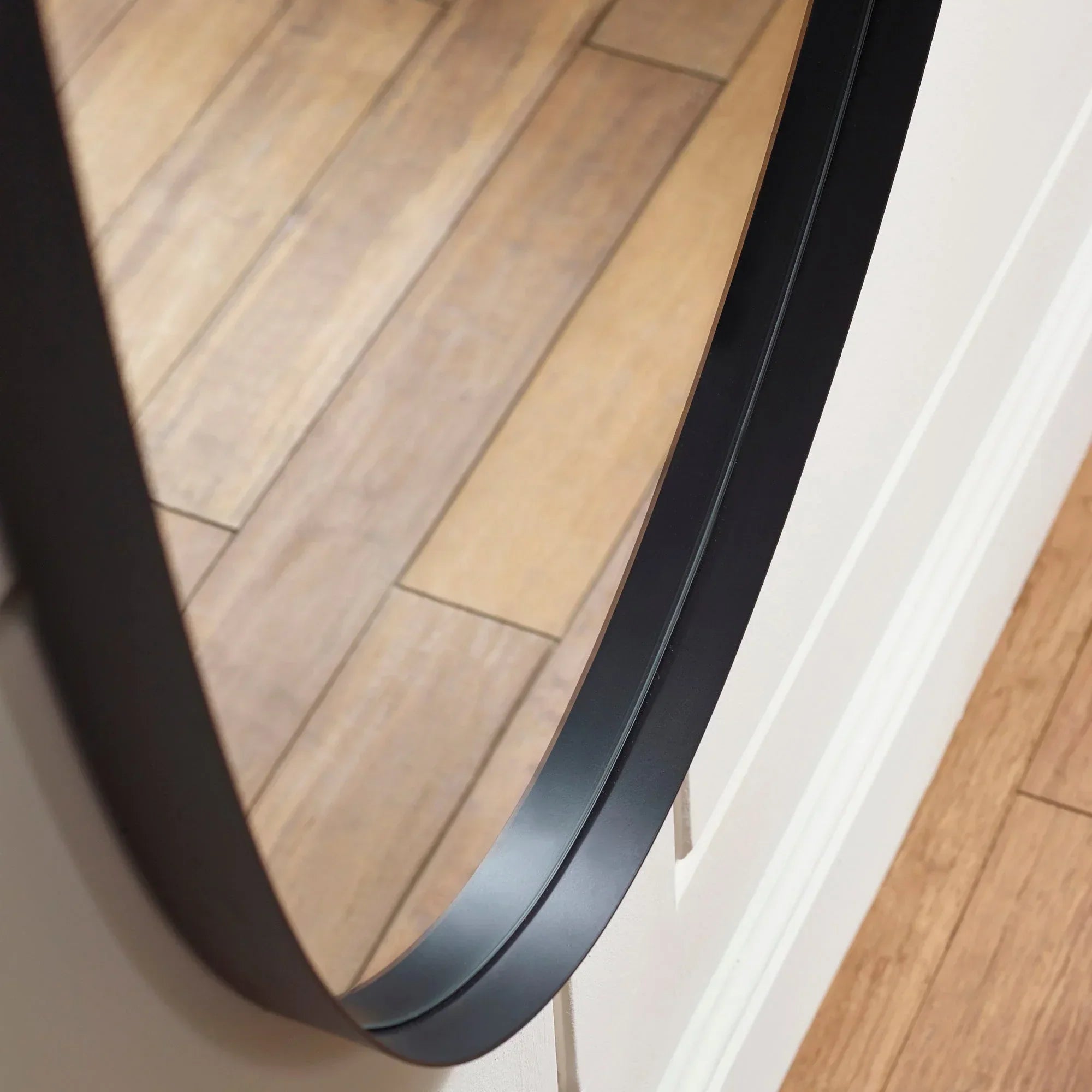 Black round mirror with slim frame close-up showing wood flooring reflection