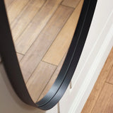 Black round mirror with slim frame close-up showing wood flooring reflection