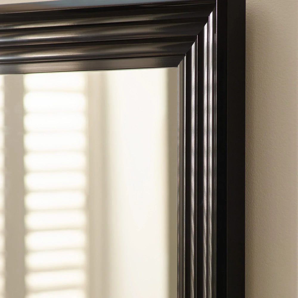 Close-up of black wooden mirror frame with grooved detailing against cream wall