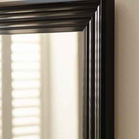 Close-up of black wooden mirror frame with grooved detailing against cream wall