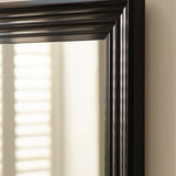 Close-up of black wooden mirror frame with grooved detailing against cream wall