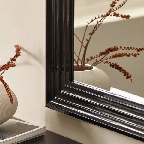 Black mirror frame close-up with ribbed ceramic vase and dried stems reflected