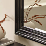 Black mirror frame close-up with ribbed ceramic vase and dried stems reflected