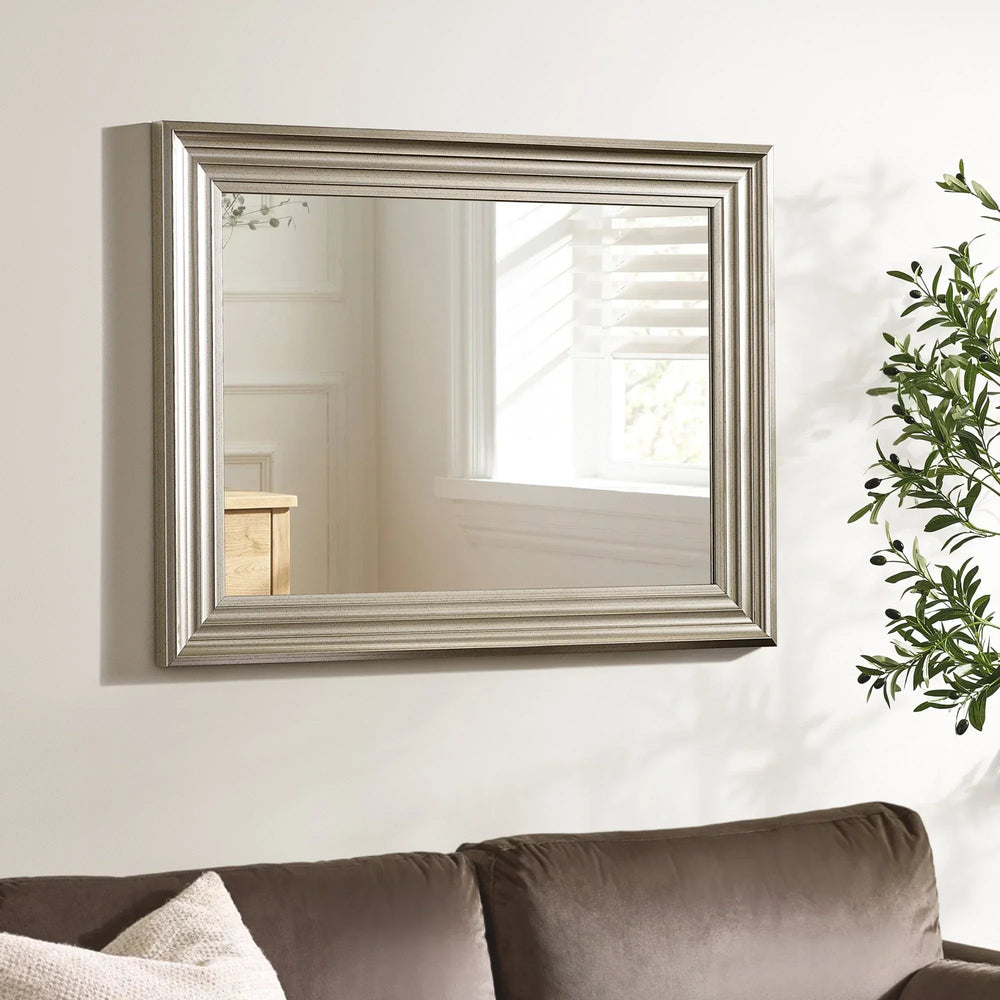 Silver wall mirror with wide beveled frame above brown sofa in living room setting