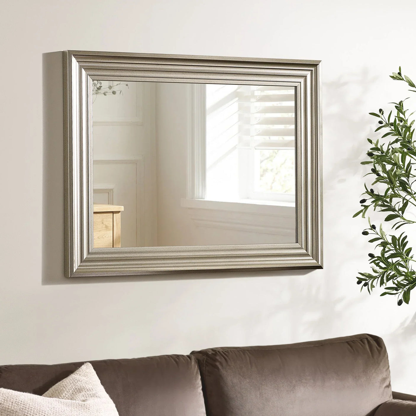Silver wall mirror with wide beveled frame above brown sofa in living room setting