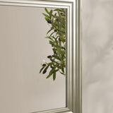 Silver wall mirror with grooved frame reflecting green leafy plant