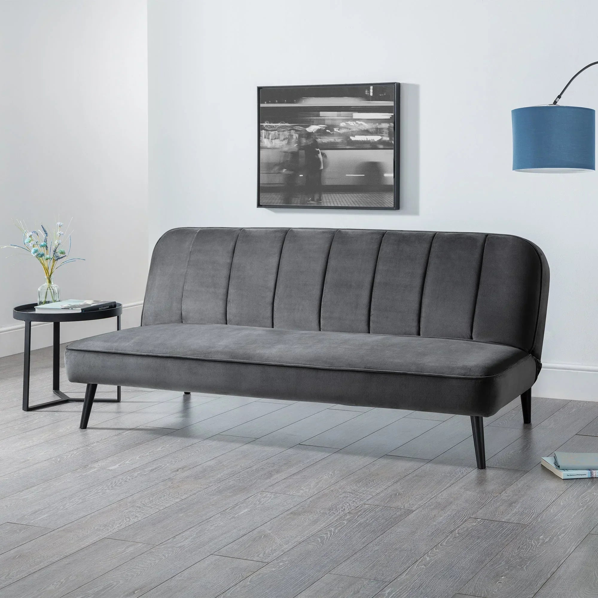 Grey velvet sofa bed with vertical stitching in modern living room, next to round side table