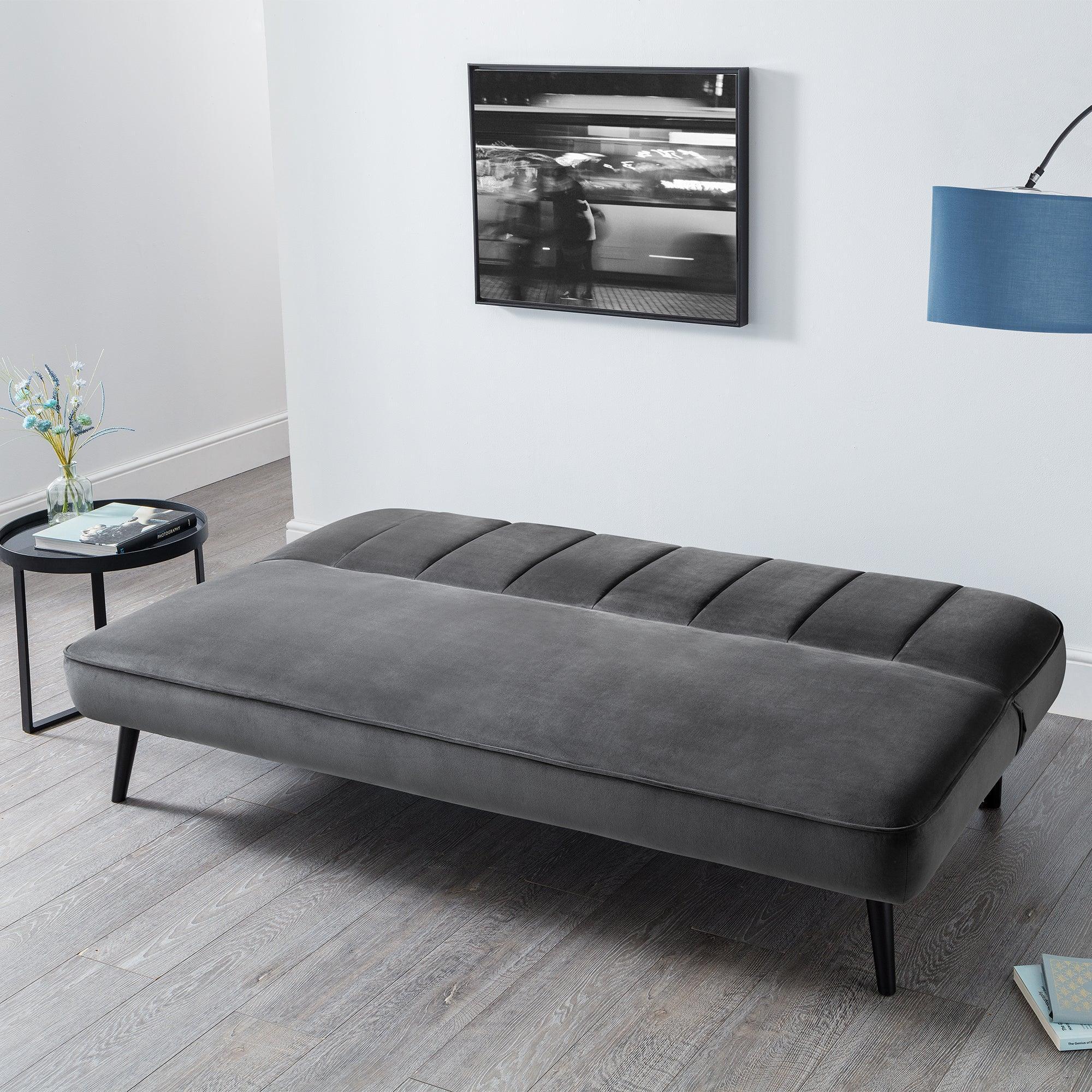 Grey velvet sofa bed with tufted top and black legs in modern living room setting
