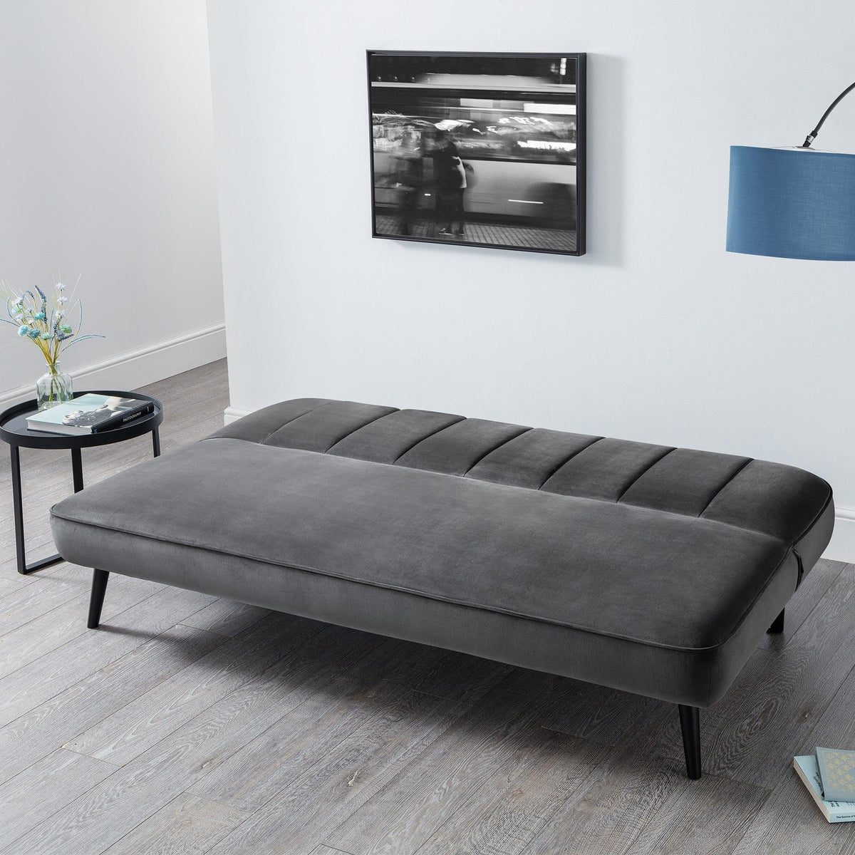 Grey velvet sofa bed with tufted top and black legs in modern living room setting