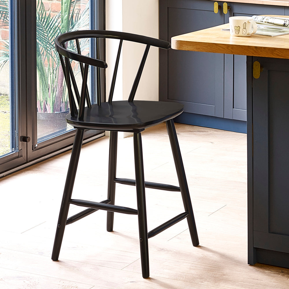 Black wooden bar stool with rounded spindle backrest in a kitchen with wood floor and blue cabinets