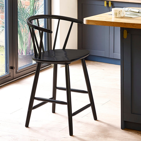 Black wooden bar stool with rounded spindle backrest in a kitchen with wood floor and blue cabinets