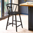 Black wooden bar stool with rounded spindle backrest in a kitchen with wood floor and blue cabinets