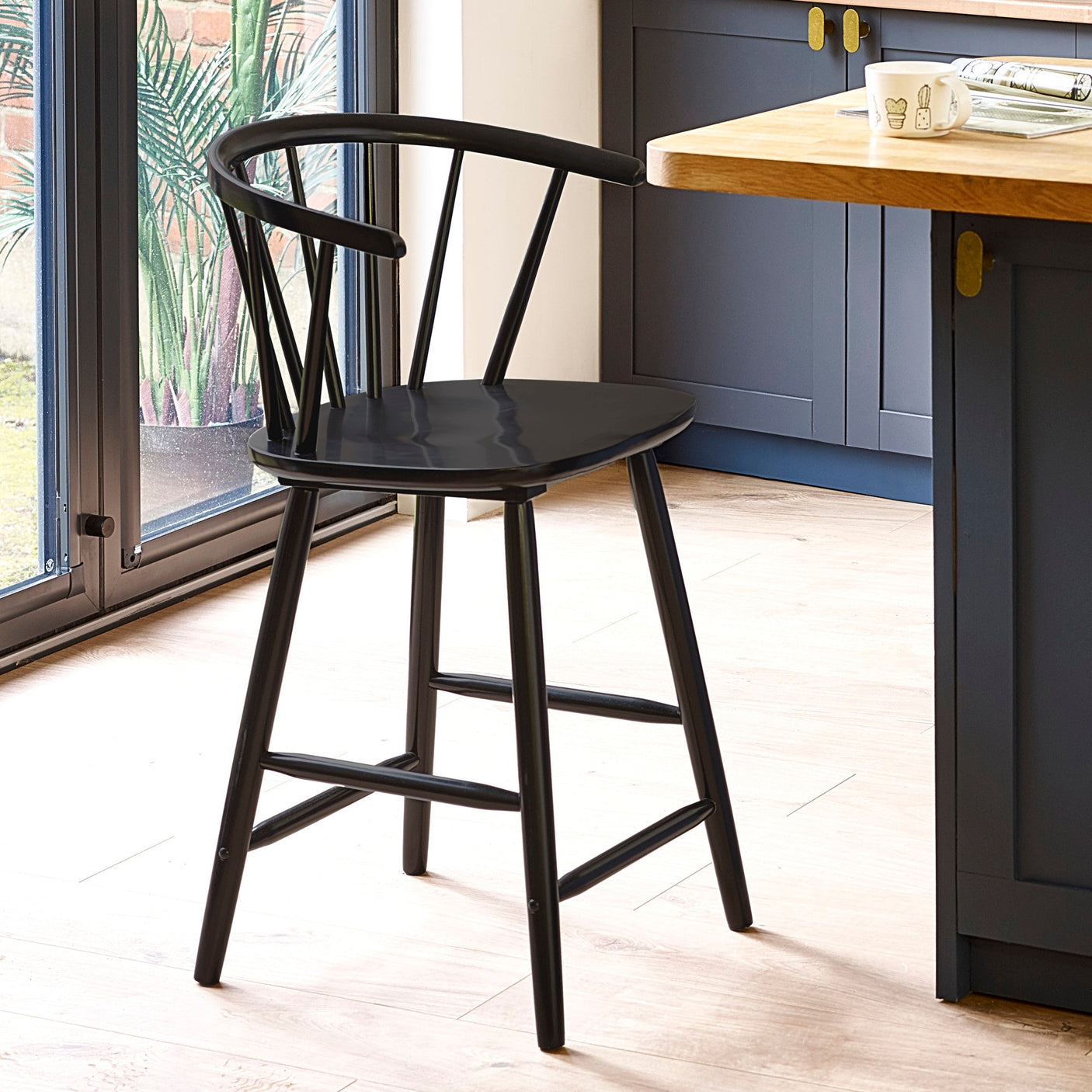 Black wooden bar stool with rounded spindle backrest in a kitchen with wood floor and blue cabinets
