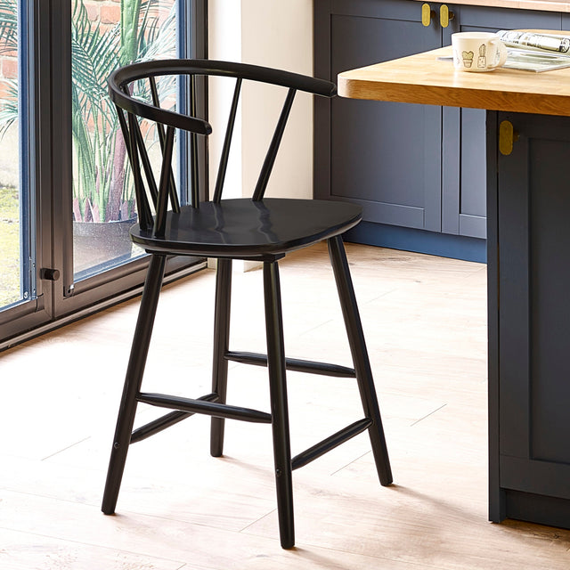 Black wooden bar stool with rounded spindle backrest in a kitchen with wood floor and blue cabinets