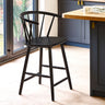 Black wooden bar stool with rounded spindle backrest in a kitchen with wood floor and blue cabinets