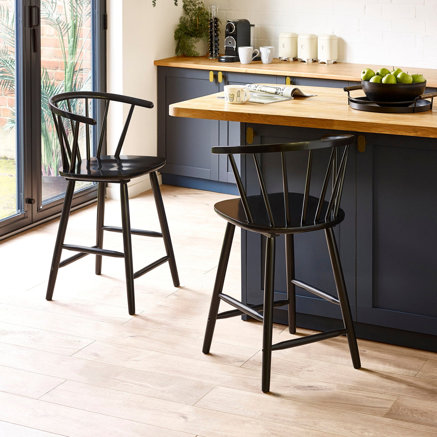 Two black wooden bar stools with rounded spindle backrests by a kitchen island with wood countertop